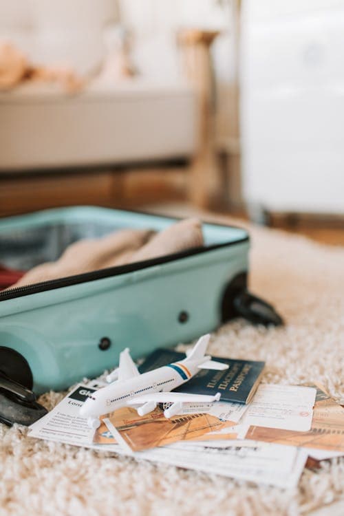 An open suitcase on a rug with a passport, boarding passes and a toy plane beside it