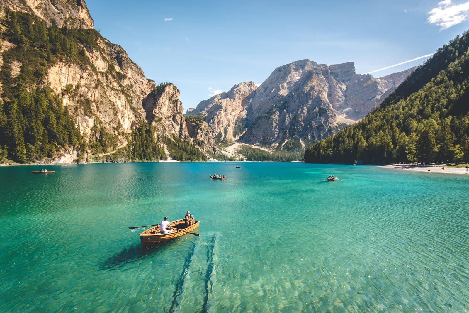 Wooden rowboats on a turquoise alpine lake ringed by pine forest and limestone peaks