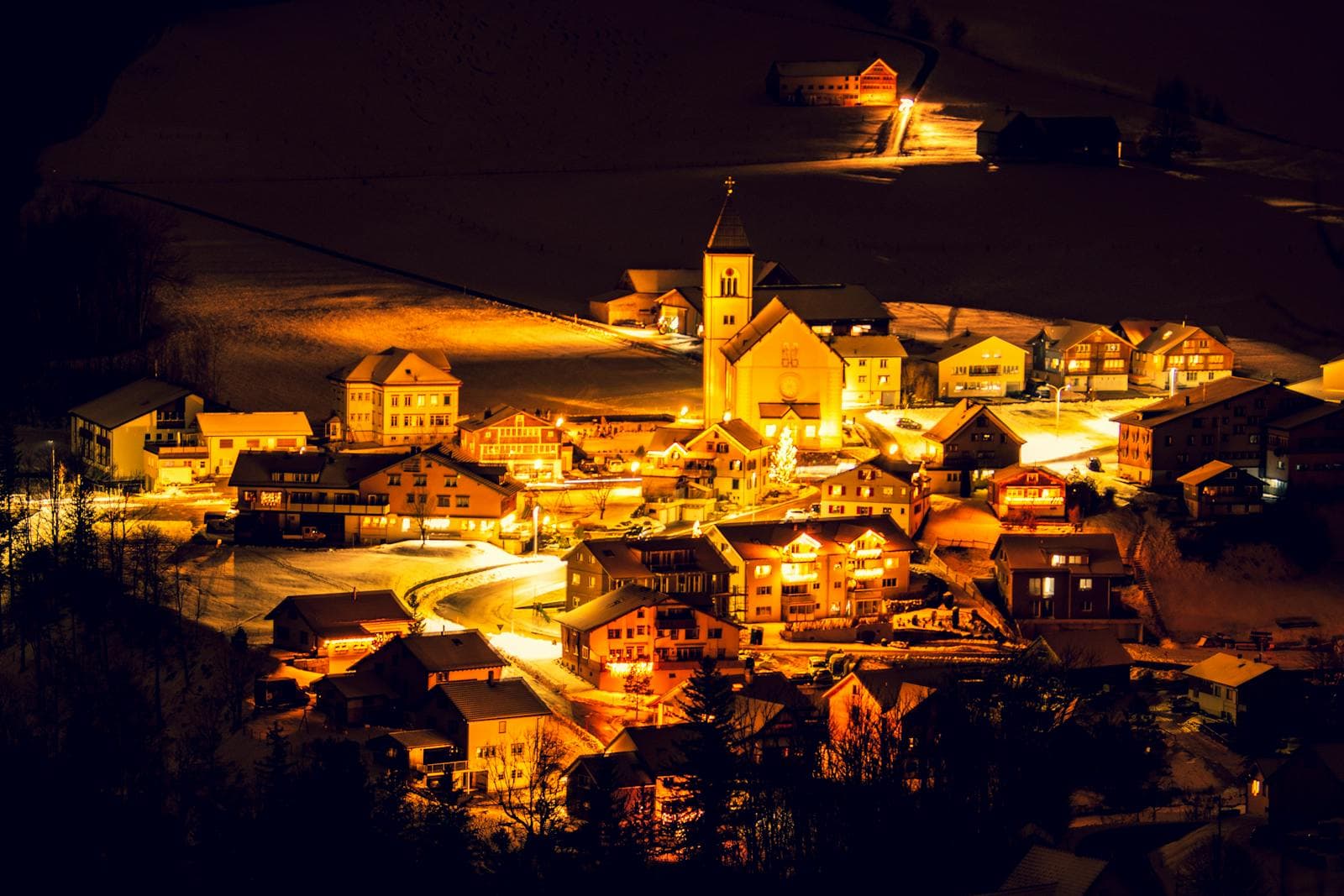 An alpine village of chalets and a church steeple lit gold against snowy slopes at night