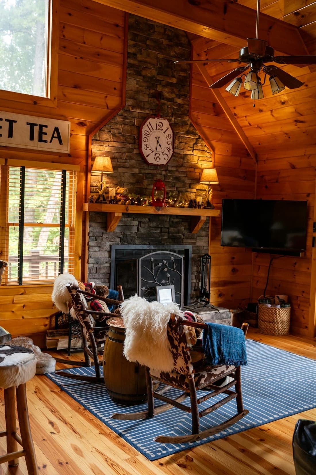 A pine-panelled cabin lounge with rocking chairs, sheepskin throws and a stone fireplace