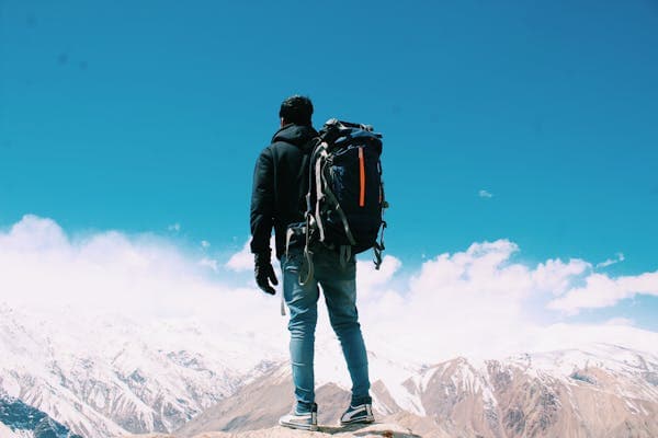 A hiker with a large pack standing on a rock above a range of snow-covered mountains